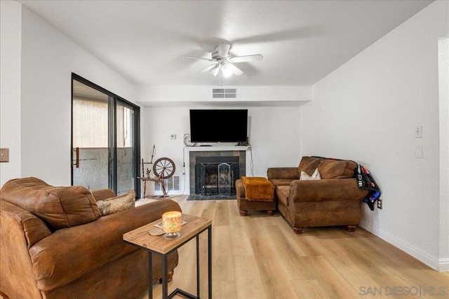 living room with ceiling fan, a tiled fireplace, and light hardwood / wood-style floors