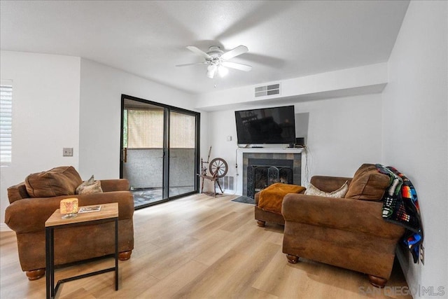 living room featuring ceiling fan, a wealth of natural light, a tile fireplace, and light hardwood / wood-style flooring