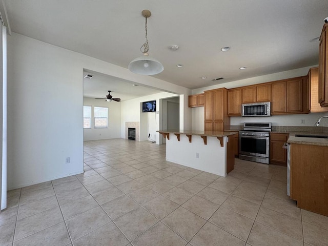 kitchen with light tile patterned floors, a kitchen bar, ceiling fan, stainless steel appliances, and decorative light fixtures