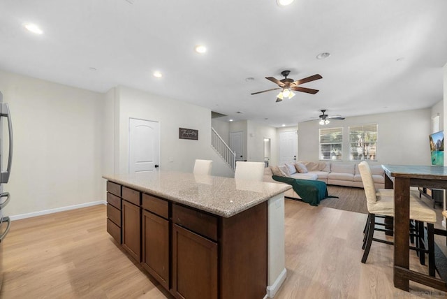 kitchen with ceiling fan, dark brown cabinetry, light stone counters, and light hardwood / wood-style floors