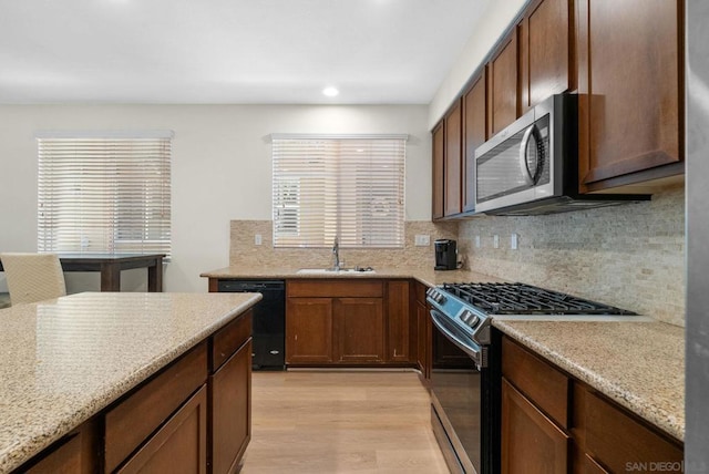 kitchen featuring tasteful backsplash, light hardwood / wood-style floors, sink, light stone countertops, and stainless steel appliances