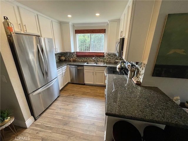 kitchen with white cabinetry, stainless steel appliances, light wood-type flooring, dark stone countertops, and sink