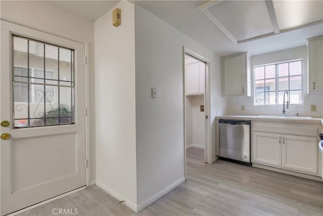 kitchen featuring tile counters, dishwasher, white cabinets, light hardwood / wood-style flooring, and sink