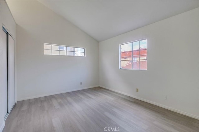 unfurnished bedroom with light wood-type flooring, vaulted ceiling, and a closet