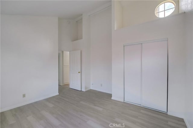 unfurnished bedroom with a high ceiling, a closet, and light wood-type flooring