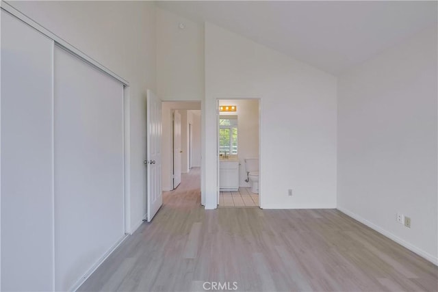 unfurnished bedroom with ensuite bath, light hardwood / wood-style flooring, a closet, and high vaulted ceiling