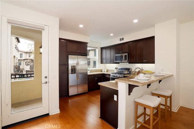 kitchen with hardwood / wood-style floors, a kitchen breakfast bar, stainless steel appliances, and dark brown cabinetry