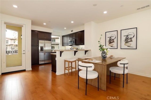 kitchen with a kitchen bar, kitchen peninsula, hardwood / wood-style flooring, stainless steel appliances, and dark brown cabinets