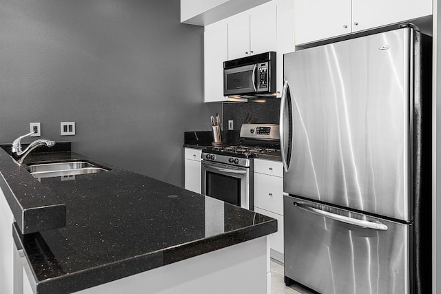 kitchen with white cabinets, stainless steel appliances, dark stone counters, sink, and kitchen peninsula