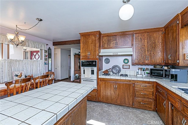 kitchen featuring tile counters, an inviting chandelier, white appliances, and pendant lighting