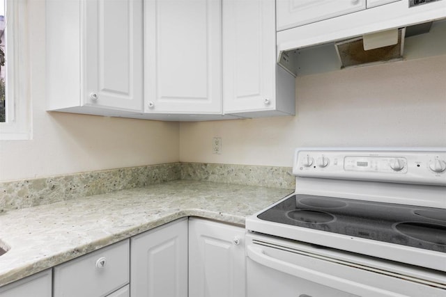 kitchen with white cabinetry, light stone countertops, and white electric range