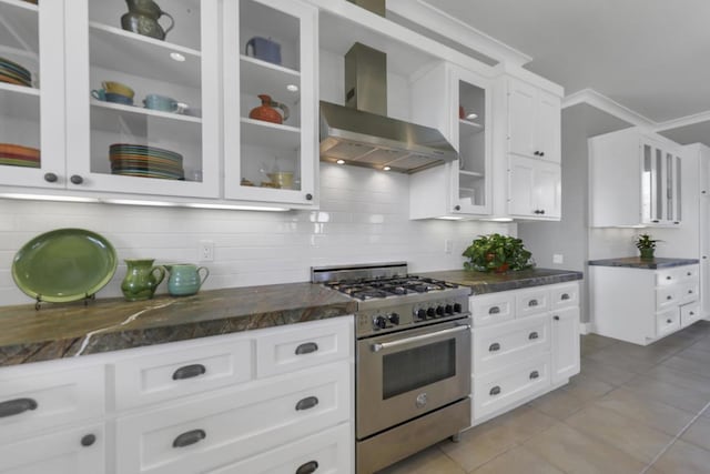 kitchen with wall chimney range hood, light tile patterned floors, high end stove, white cabinets, and decorative backsplash