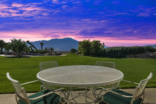 patio terrace at dusk featuring a mountain view and a lawn