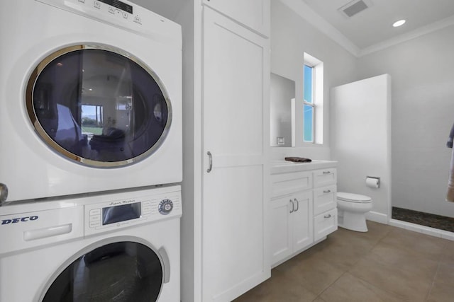 washroom featuring dark tile patterned floors, stacked washing maching and dryer, and ornamental molding