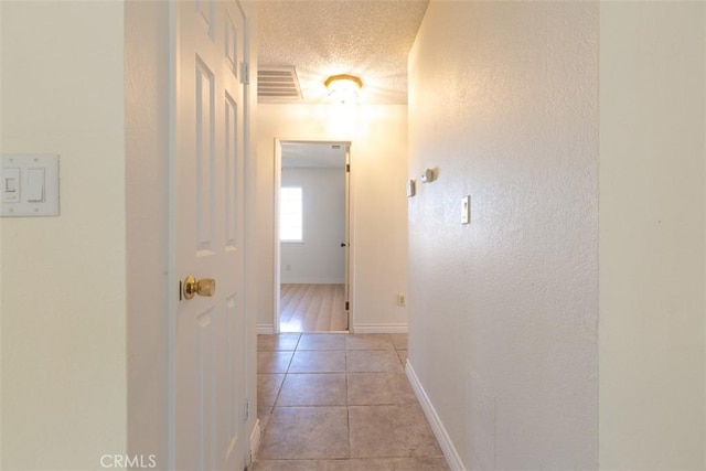 hall with a textured ceiling and light tile patterned flooring