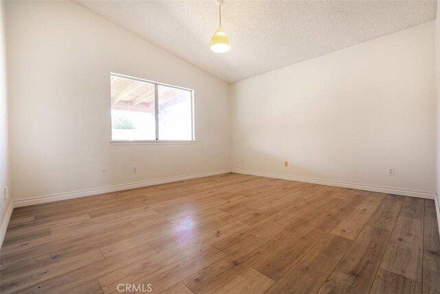 spare room featuring a textured ceiling, light wood-type flooring, and vaulted ceiling