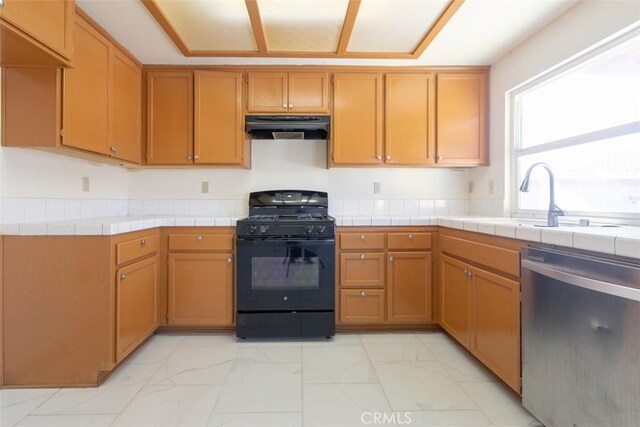 kitchen with tile countertops, stainless steel dishwasher, black gas stove, and sink