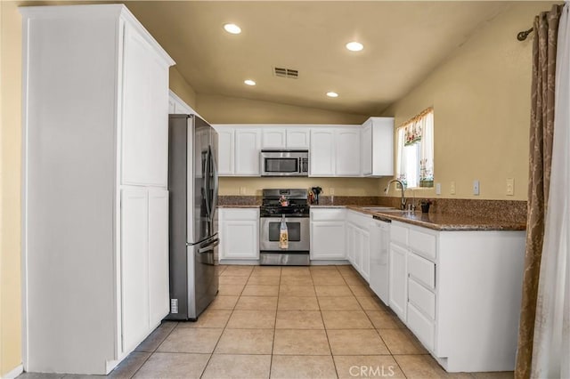 kitchen featuring white cabinets, lofted ceiling, stainless steel appliances, dark stone counters, and light tile patterned floors