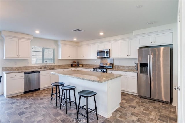 kitchen with appliances with stainless steel finishes, white cabinetry, a kitchen island, and a kitchen bar