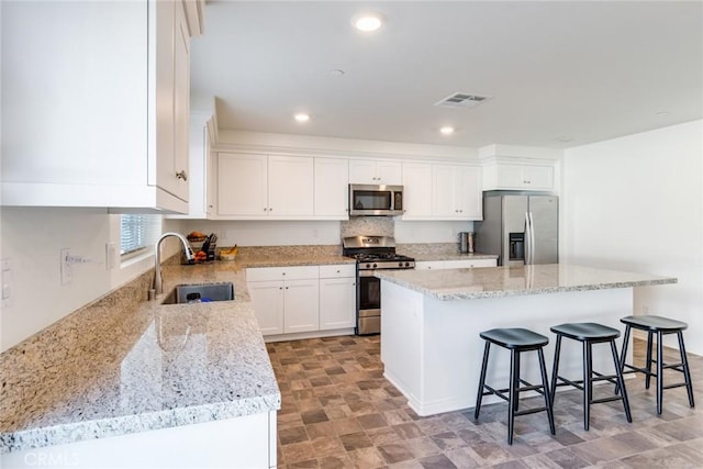 kitchen with a sink, appliances with stainless steel finishes, a kitchen island, and white cabinetry