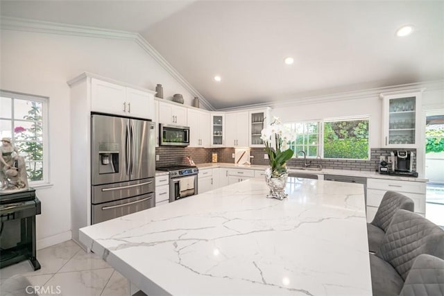 kitchen with a kitchen bar, appliances with stainless steel finishes, tasteful backsplash, light stone countertops, and vaulted ceiling