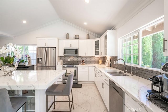 kitchen featuring vaulted ceiling, sink, a kitchen breakfast bar, stainless steel appliances, and white cabinets