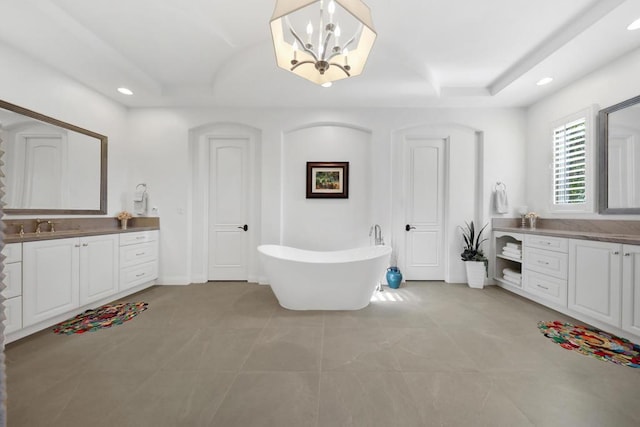 bathroom featuring tile patterned flooring, vanity, a bath, a raised ceiling, and a chandelier