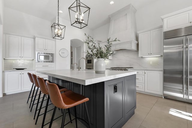 kitchen featuring pendant lighting, built in appliances, a center island with sink, and white cabinets