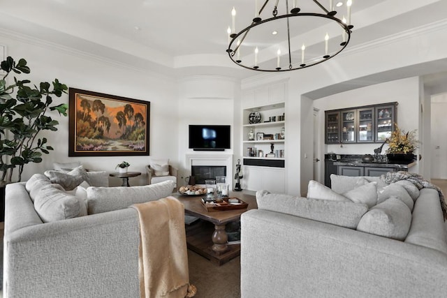 living room featuring ornamental molding, built in features, and a chandelier