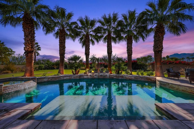 pool at dusk with an in ground hot tub and a mountain view