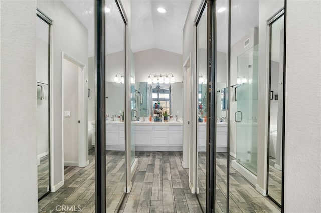 bathroom with vaulted ceiling, a textured ceiling, walk in shower, and vanity