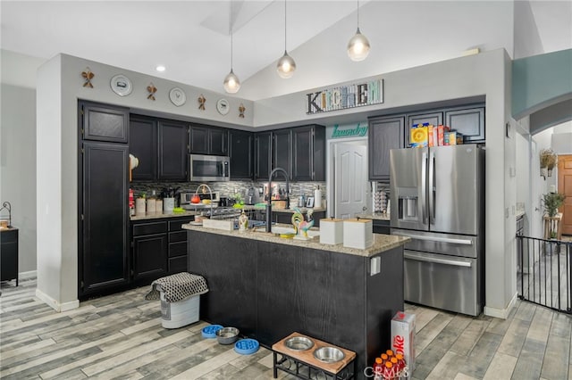 kitchen with pendant lighting, stainless steel appliances, tasteful backsplash, an island with sink, and light stone counters