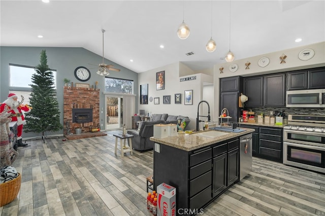 kitchen featuring backsplash, sink, light stone countertops, an island with sink, and stainless steel appliances