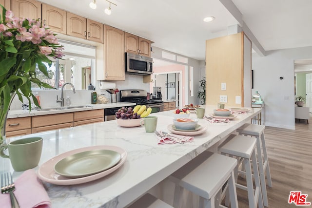 kitchen with light hardwood / wood-style floors, a breakfast bar area, appliances with stainless steel finishes, decorative backsplash, and light brown cabinetry