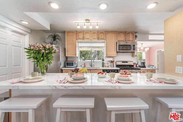 kitchen with a breakfast bar area, stainless steel appliances, light brown cabinets, and sink