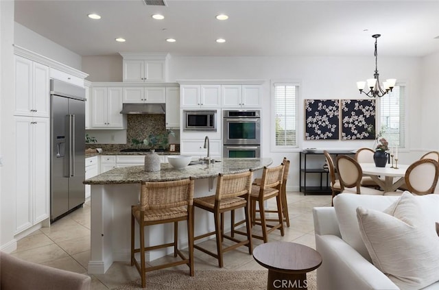 kitchen featuring a wealth of natural light, white cabinetry, dark stone counters, built in appliances, and light tile patterned floors