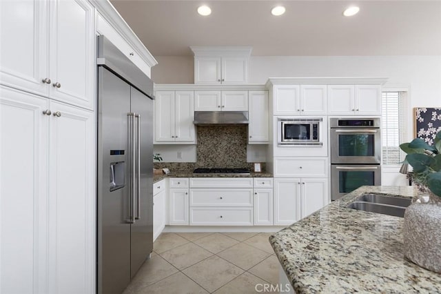 kitchen with light stone countertops, white cabinetry, built in appliances, backsplash, and light tile patterned floors