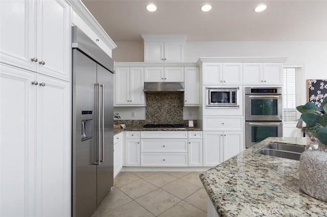 kitchen with light tile patterned flooring, light stone counters, tasteful backsplash, built in appliances, and white cabinets