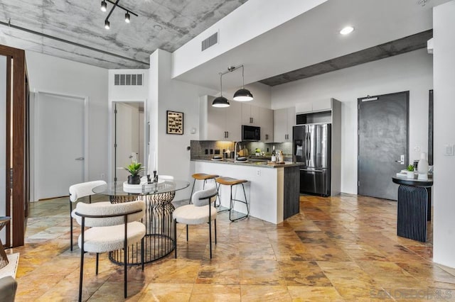 kitchen featuring stainless steel fridge with ice dispenser, kitchen peninsula, a breakfast bar area, tasteful backsplash, and decorative light fixtures