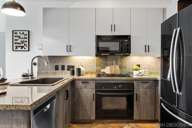 kitchen with light stone counters, sink, white cabinets, and black appliances