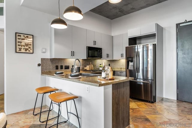 kitchen with tasteful backsplash, sink, hanging light fixtures, stainless steel fridge, and kitchen peninsula