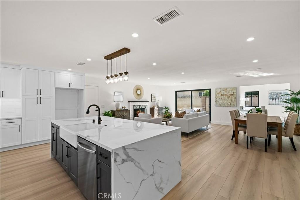 kitchen featuring an island with sink, light stone countertops, pendant lighting, stainless steel dishwasher, and sink