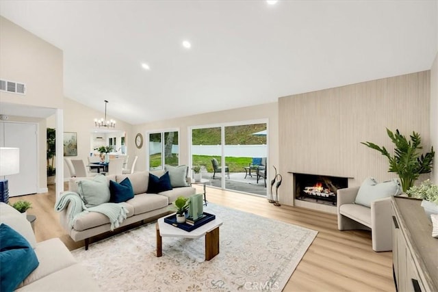 living room with light wood-type flooring, a chandelier, vaulted ceiling, and a fireplace