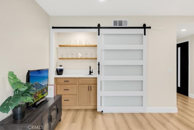 bar with sink, light brown cabinets, a barn door, and light wood-type flooring