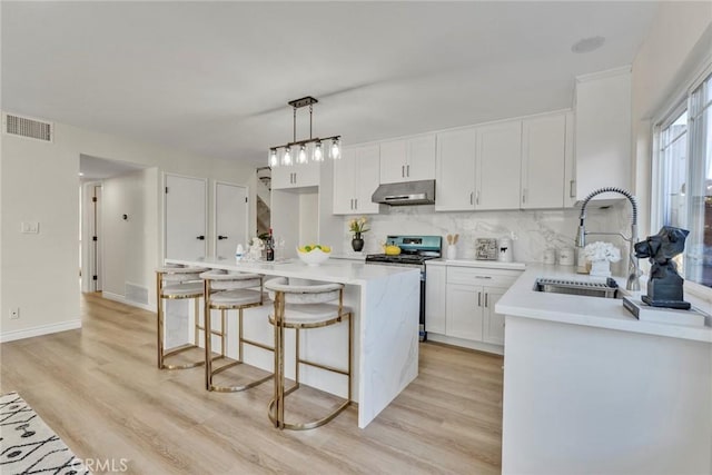 kitchen with a center island, stainless steel gas range oven, sink, white cabinetry, and hanging light fixtures