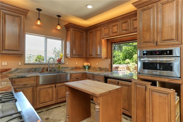 kitchen with pendant lighting, sink, light stone countertops, a center island, and stainless steel oven