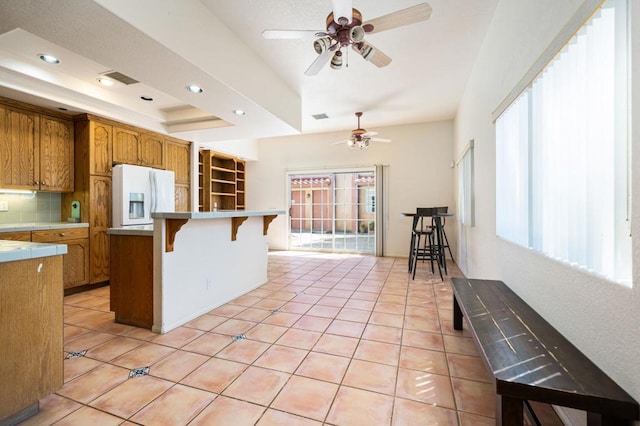 kitchen featuring a breakfast bar, white fridge with ice dispenser, light tile patterned floors, and a raised ceiling