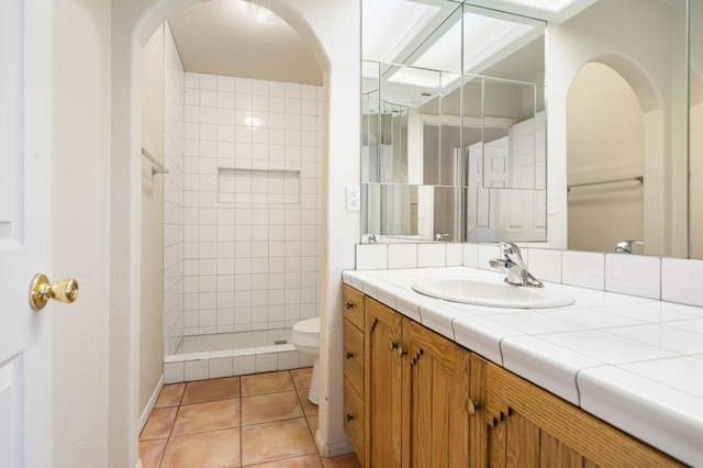 bathroom featuring toilet, tile patterned floors, tiled shower, and vanity