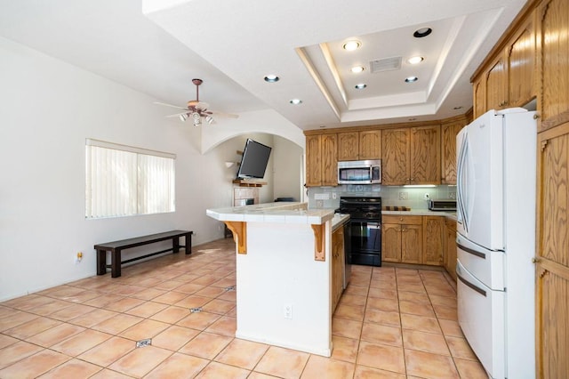 kitchen with white fridge, light tile patterned floors, ceiling fan, black gas range oven, and a raised ceiling