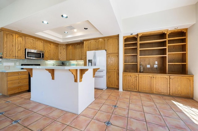 kitchen with light tile patterned floors, white fridge with ice dispenser, a tray ceiling, and a kitchen island